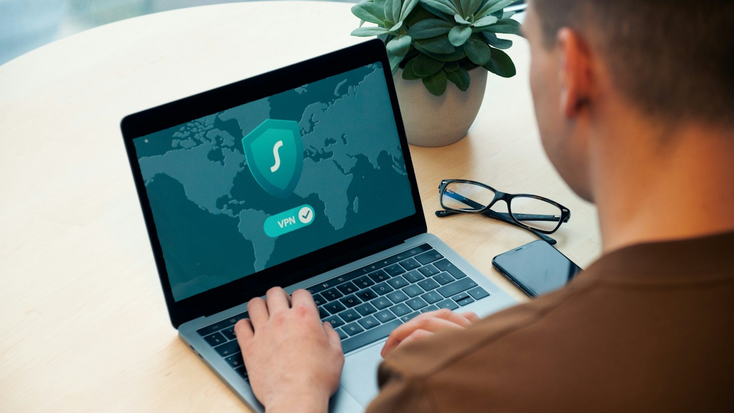 Person using a laptop with a VPN connection on a wooden desk.